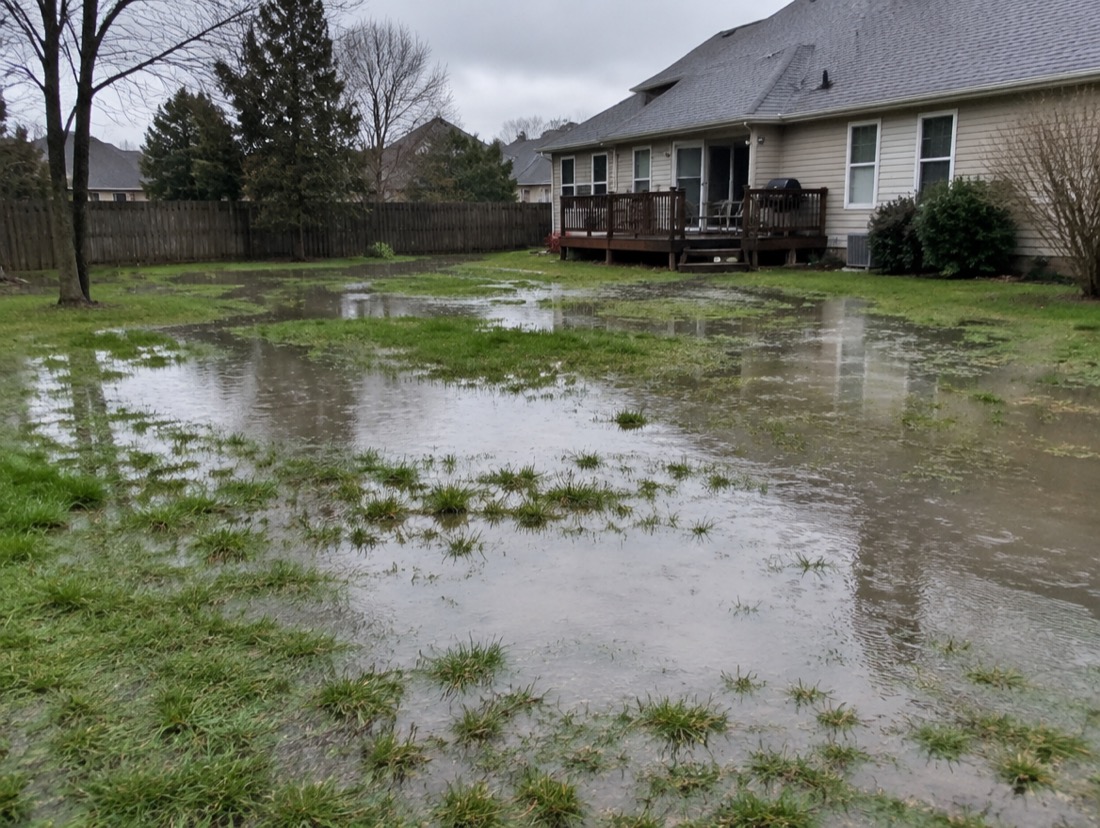 Flooded Charlotte backyard with standing water pooling across saturated red-clay soil